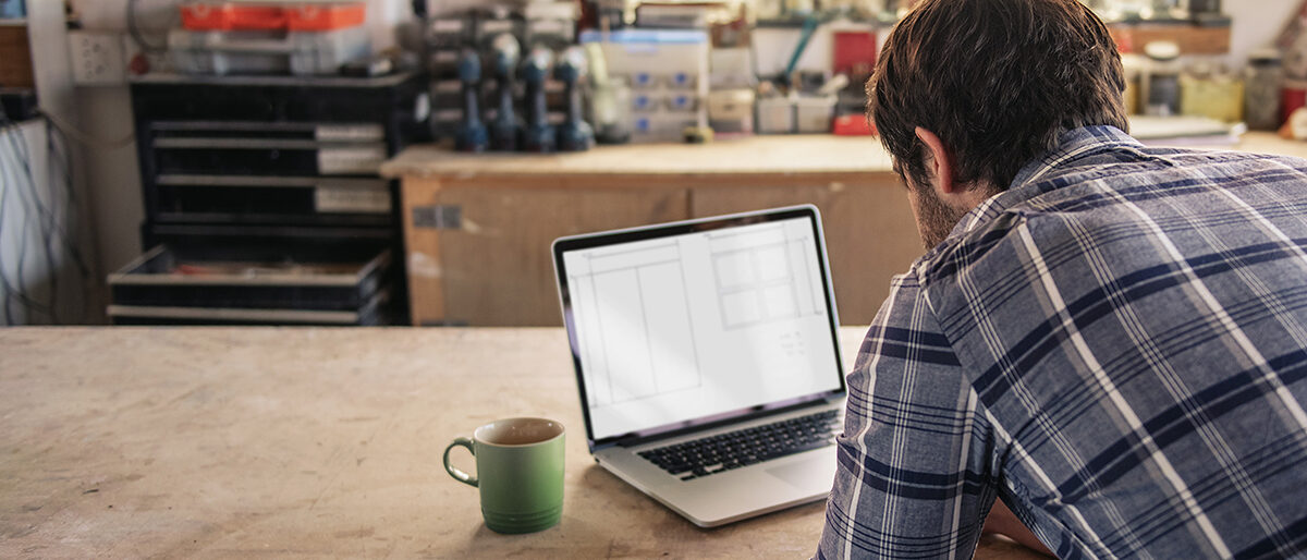 Ein Handwerker arbeitet an seinem Laptop in der Werkstatt Ein Handwerker arbeitet an seinem Laptop in der Werkstatt