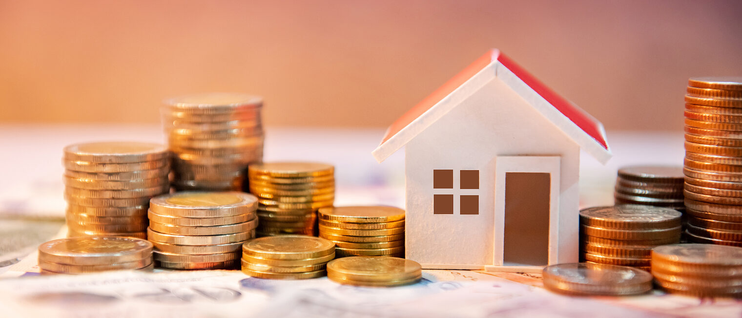 Symbolisches Hausmodell zwischen Münzstapeln auf Geldscheinen, Fokus auf Baufinanzierung oder Investitionen