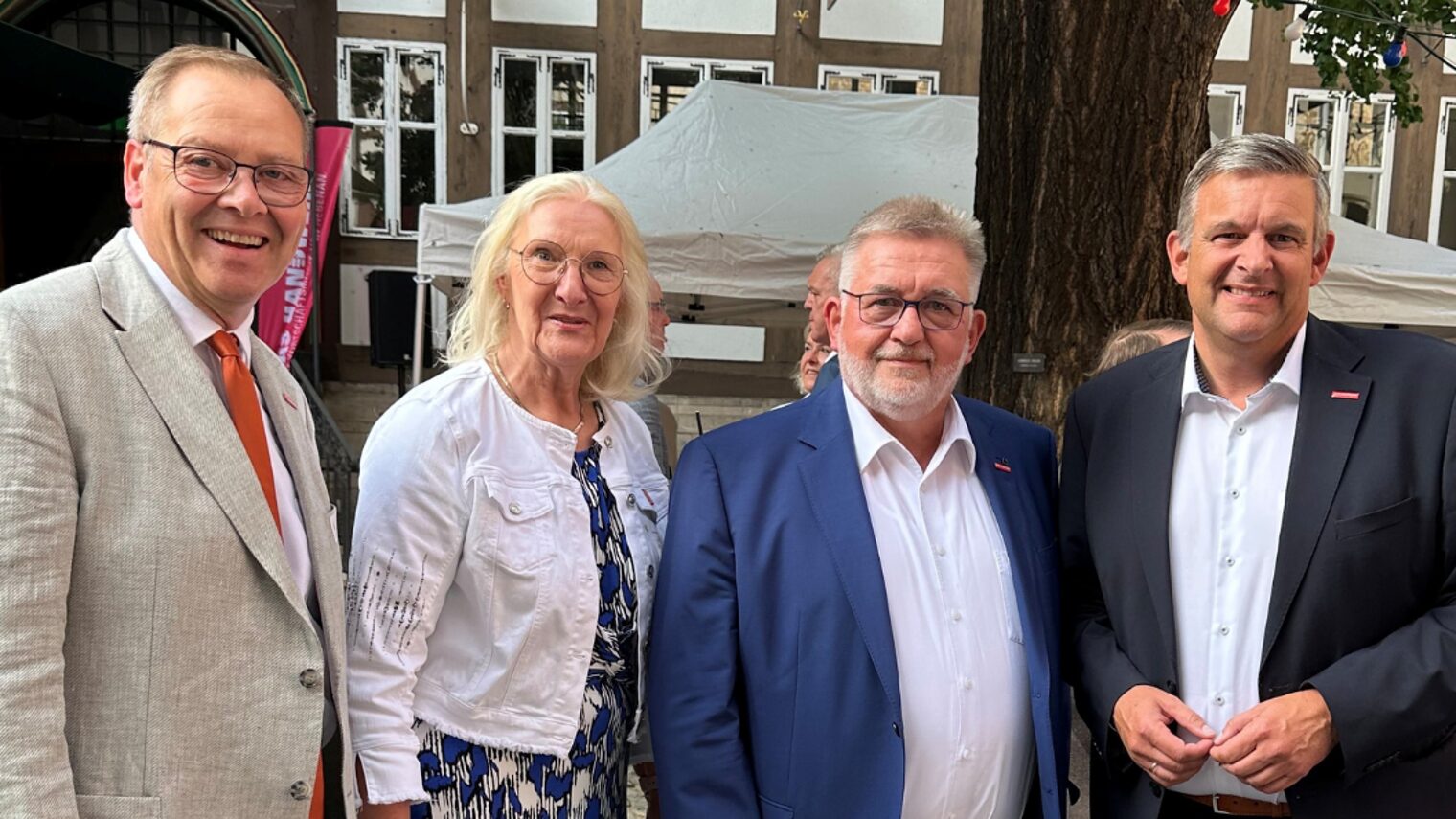 Gruppenfoto mit vier Personen im Anzug bei Veranstaltung im Freien vor Fachwerk-Kulisse und Ginkgobaum