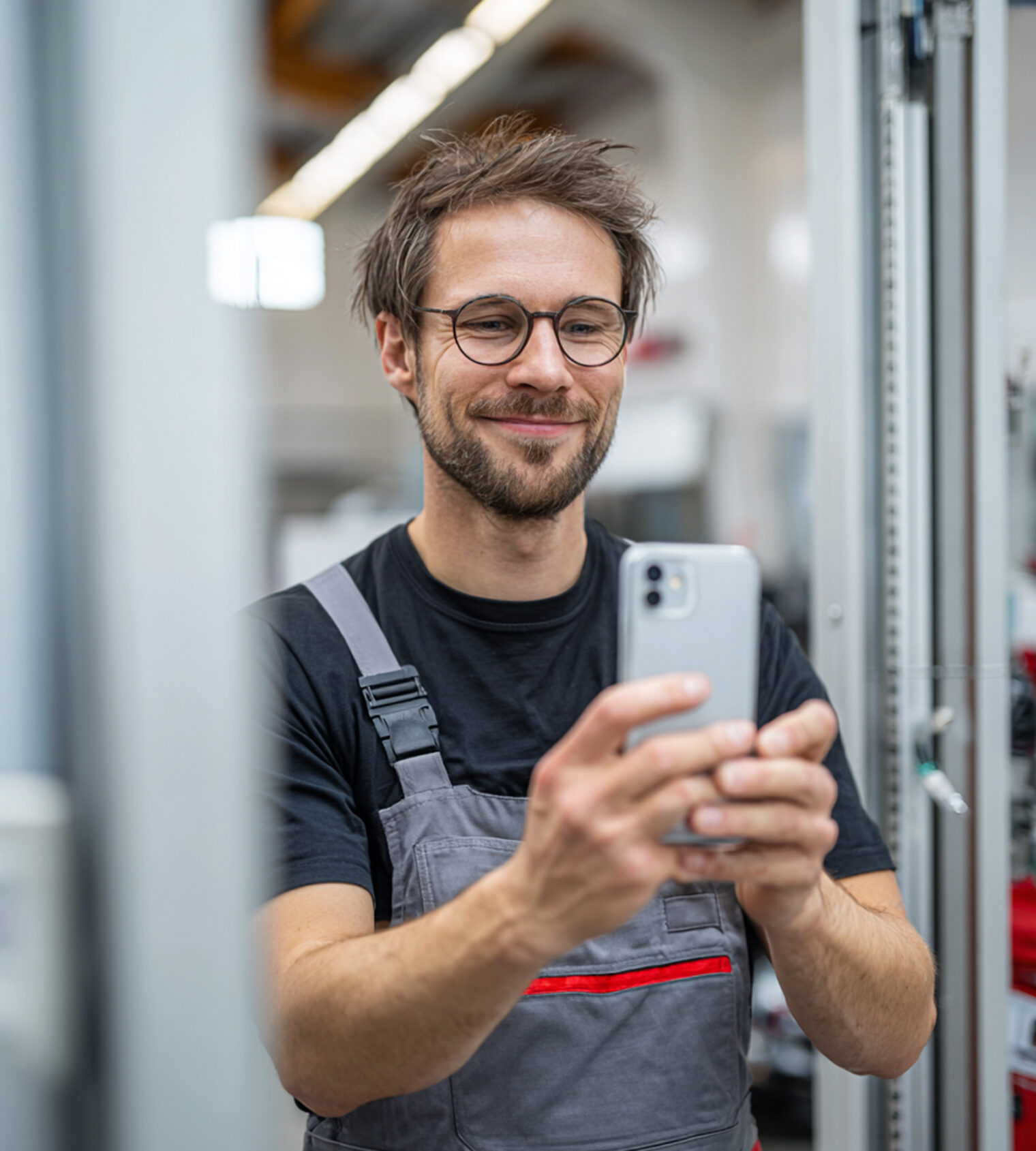 Junger Handwerker in Arbeitskleidung macht ein Selfie mit dem Smartphone in moderner Werkstatt
