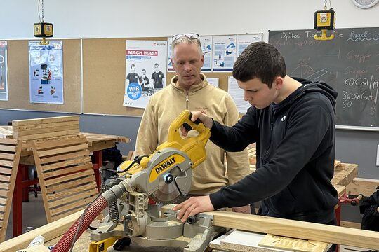Auszubildender arbeitet unter Anleitung eines Ausbilders mit einer Kappsäge an einem Holzstück