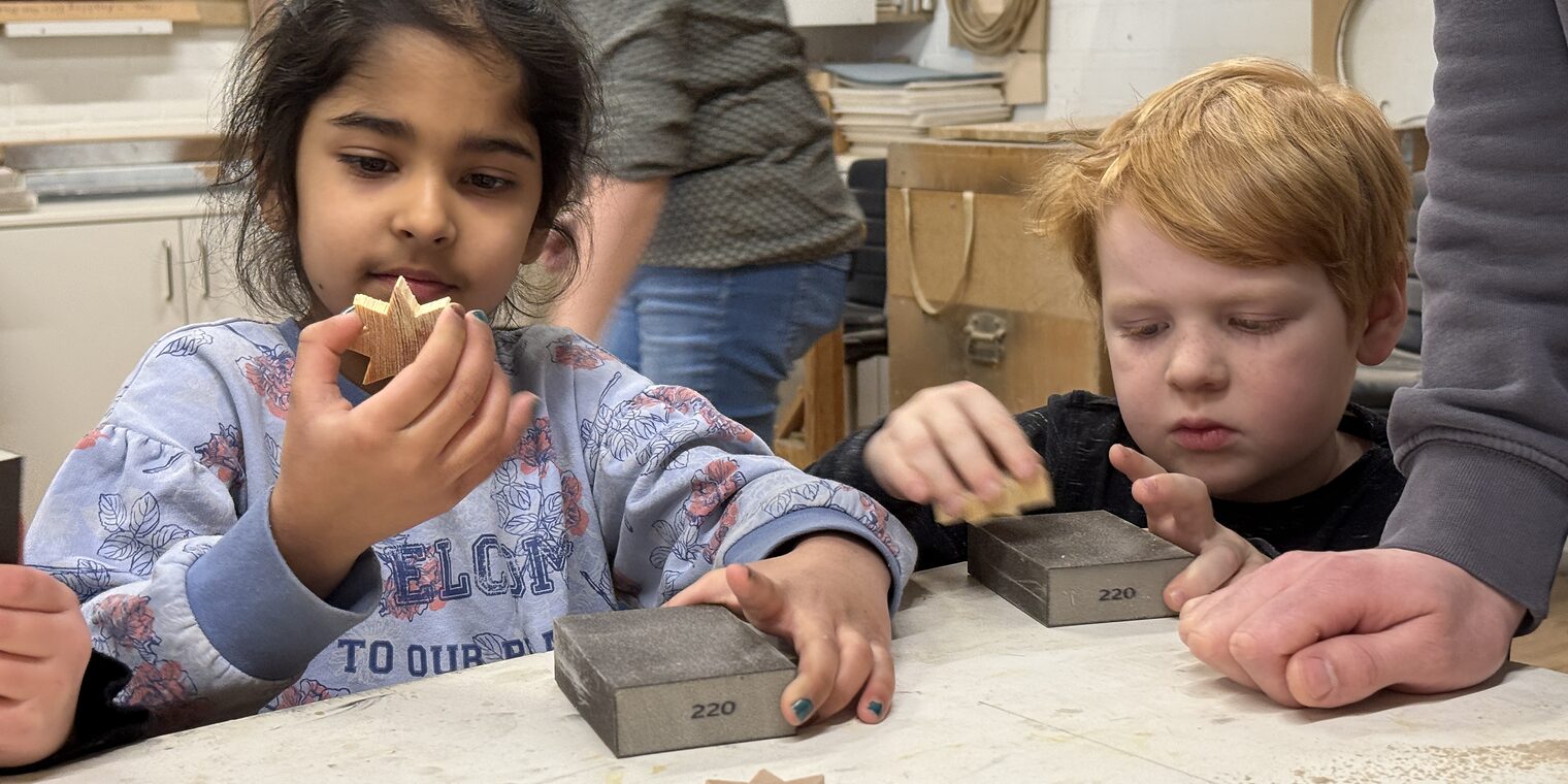 Zwei Kindergartenkinder blicken in einer Werkstatt stolz auf ihre selbst gemachten Holzsterne.